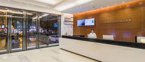 A hotel reception area with a modern design, featuring a reception desk, a television screen, and a glass entrance.