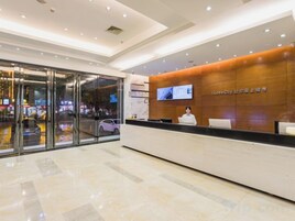 Zona de recepción de un hotel con diseño moderno, que incluye un mostrador de recepción, una pantalla de televisión y una entrada de vidrio.