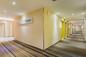 Pasillo de hotel con pisos alfombrados, puertas y un cuadro en la pared.