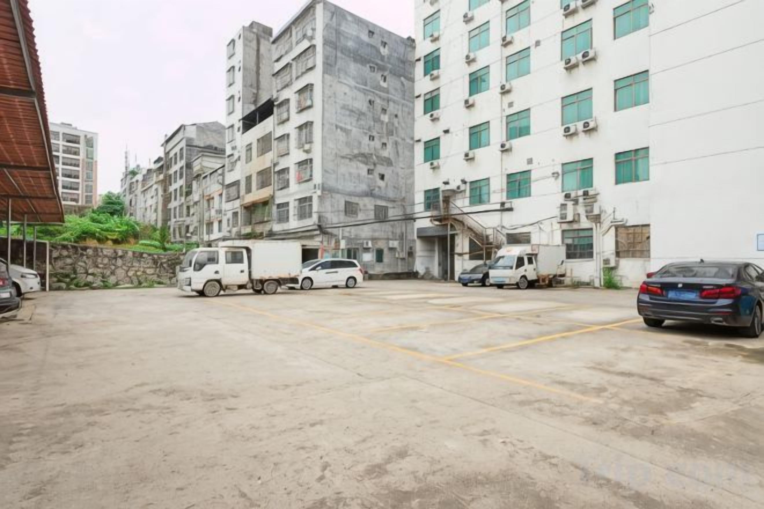 A parking lot with a white building, a truck, and a car.