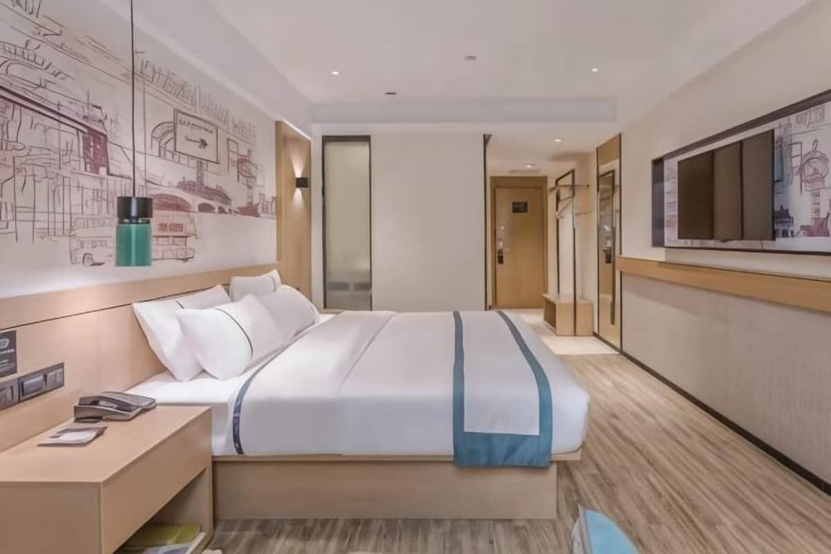 Quarto de hotel com cama, mesa de cabeceira e uma janela grande.