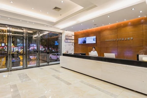 A hotel reception area with a modern design, a reception desk, and a large screen displaying information.