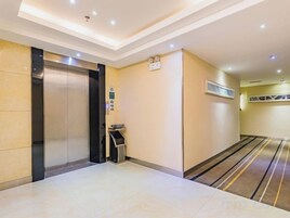 Vestíbulo de hotel con suelo de mármol, un ascensor, un cubo de basura y una zona alfombrada.