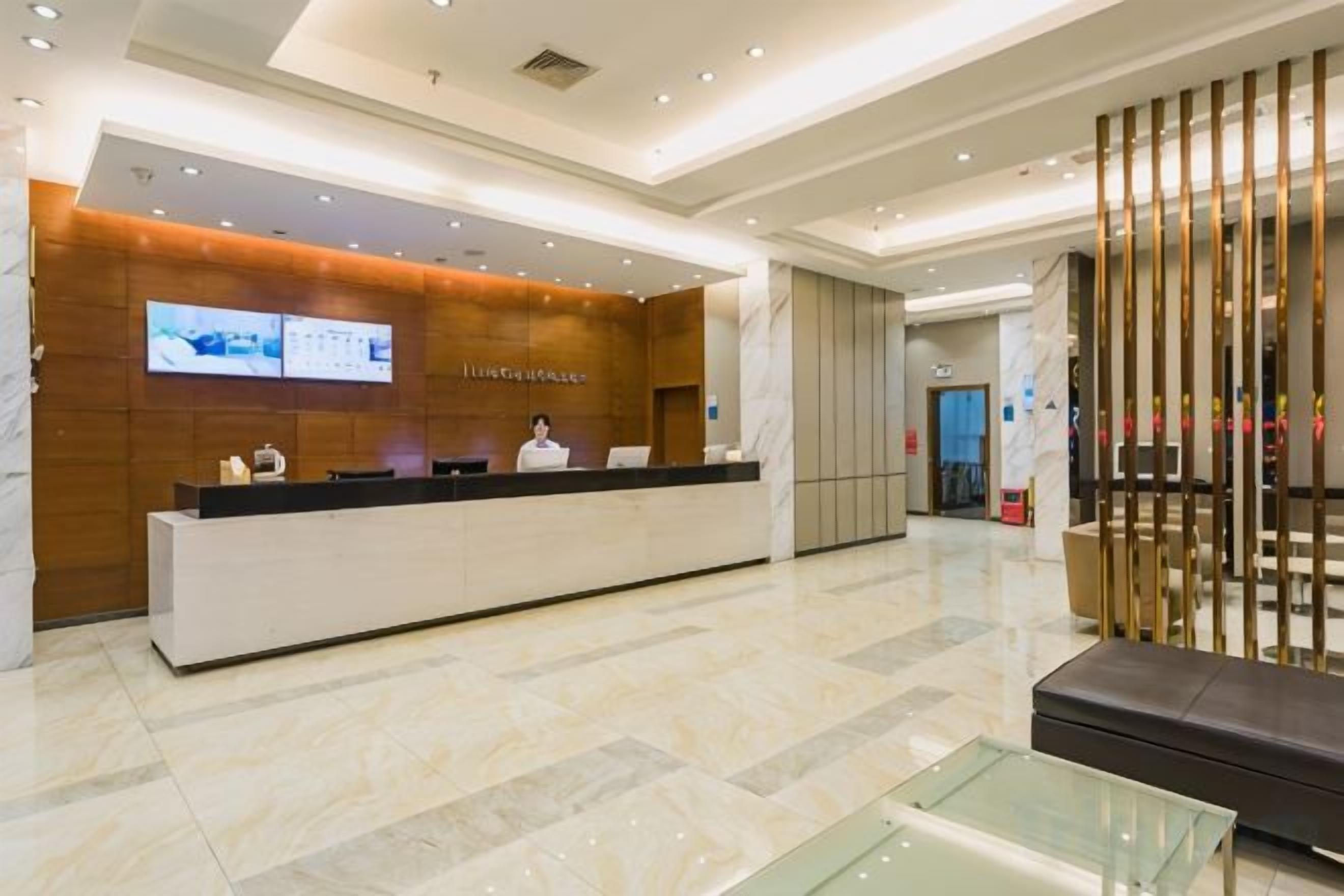A hotel reception area with a reception desk, a television screen, and a seating area with a glass table.