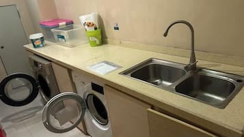 A kitchenette with a sink, a washing machine, and a small countertop with various items.