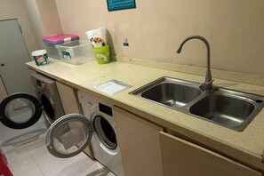Una kitchenette con un lavabo, lavadora y una pequeña encimera con diversos objetos.