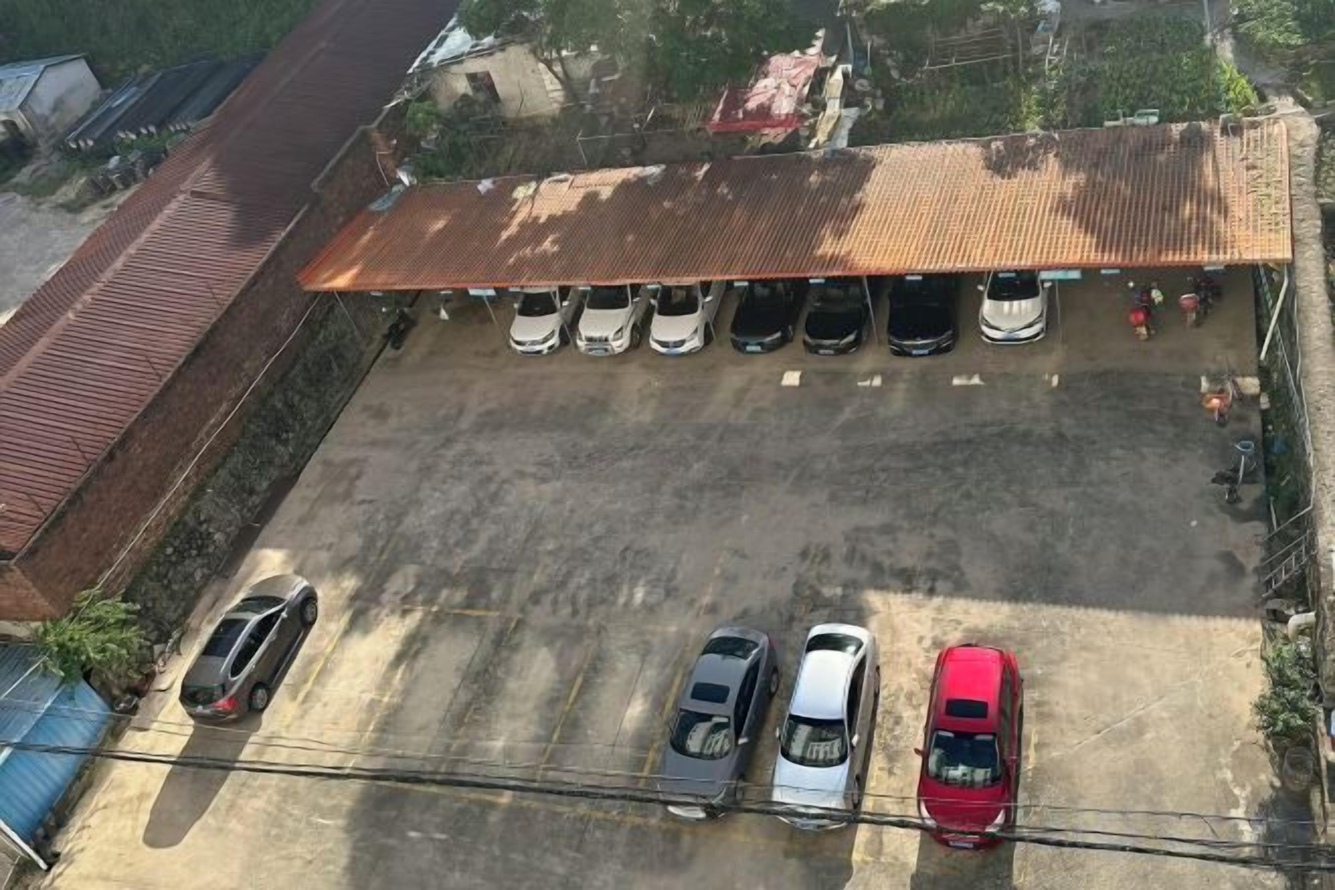 An aerial view of a parking lot with several cars, a building with a red roof, and a fenced area.