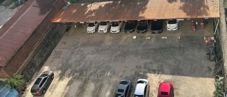 An aerial view of a parking lot with several cars, a building with a red roof, and a fenced area.