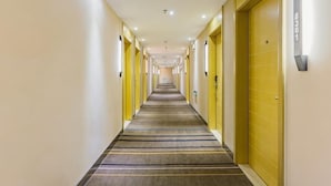 Un couloir d’hôtel avec des portes de chaque côté, un sol recouvert de moquette et un éclairage au plafond.