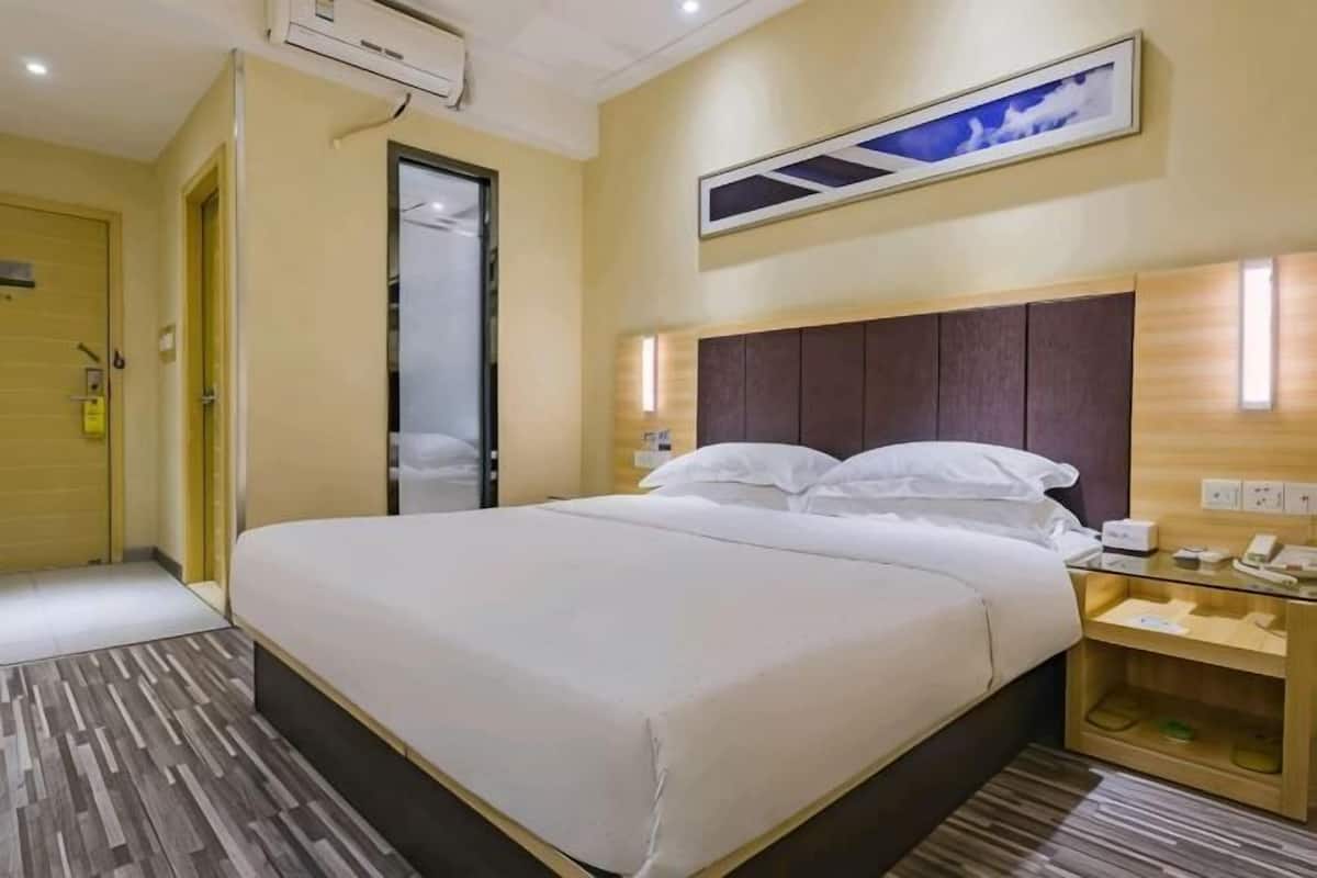 Quarto de hotel com uma cama grande, cabeceira de madeira, mesa de cabeceira e televisão fixada na parede.