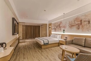 Habitación de hotel con cama, sofá, una mesita, mesita de noche y televisor montado en la pared.