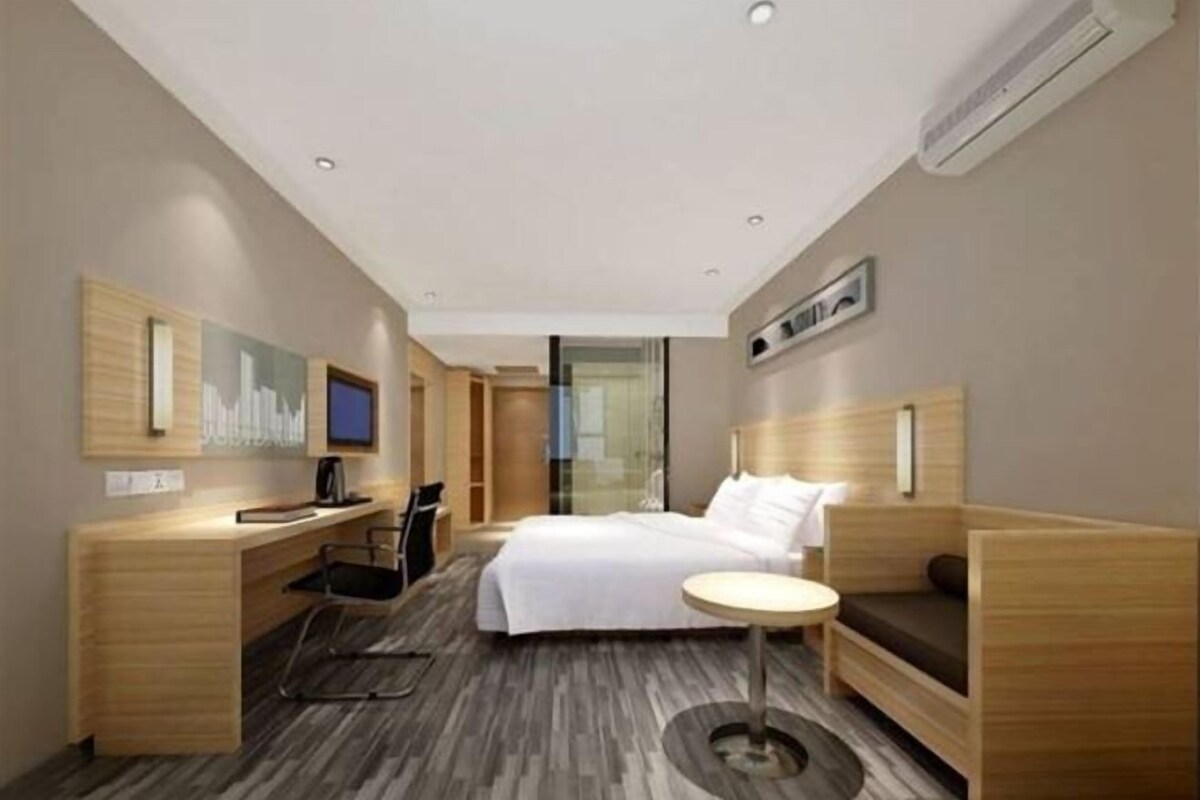 A modern hotel room with a bed, desk, chair, and a small round table.