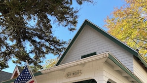 A white wooden house with a porch, an American flag, and a sign reading "DRIFTWOOD."