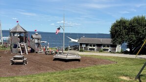 A playground with a slide, a small building, and a flagpole with an American flag.