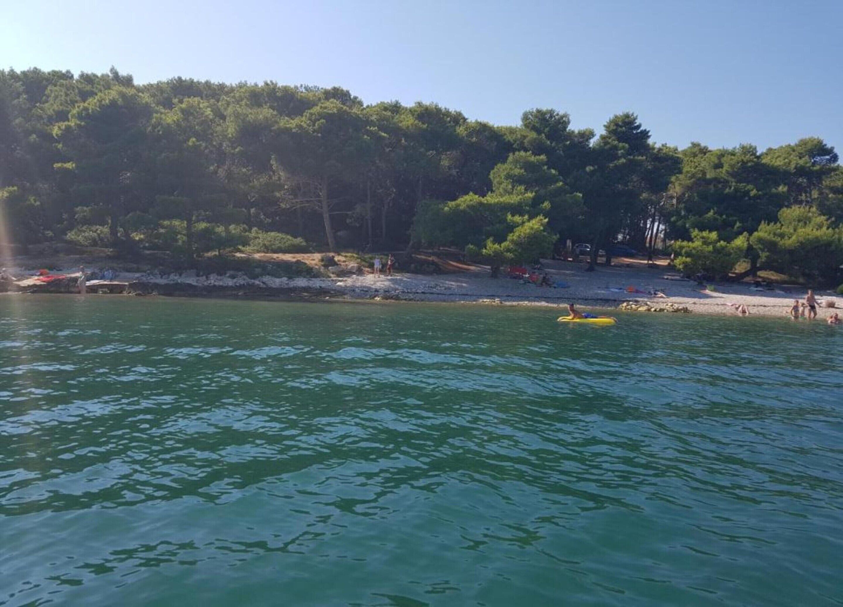 Una spiaggia con acque cristalline, alberi e persone.