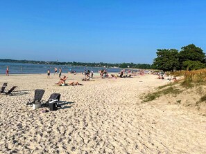 A sandy beach with lounge chairs and umbrellas, a clear sky, and a tree line in the background. - 4 Person Holiday Home in Kopingsvik (Kopingsvik)
