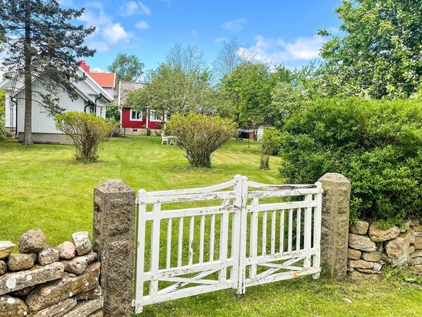 A white wooden gate with a stone wall on one side and a grassy lawn in the foreground.
