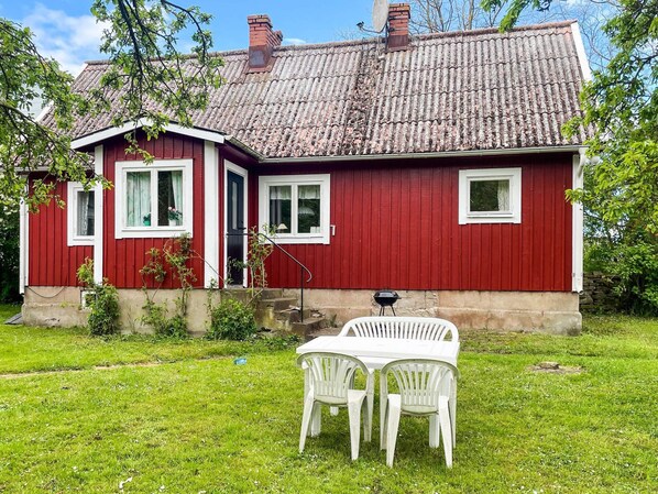 Ein rotes Haus mit weißem Zierdekor, einem Schornstein und einem kleinen Garten mit einem weißen Tisch und Stühlen.