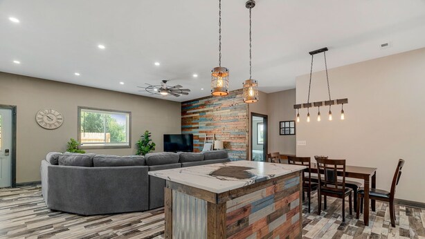 A modern kitchen with a central island, a dining area with wooden chairs, and a gray sectional sofa. - Raccoon Lake Retreat (Rockville)