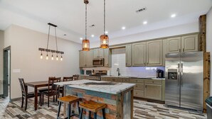A modern kitchen with wooden cabinets, a stainless steel refrigerator, and a central island with stools. - Raccoon Lake Retreat (Rockville)