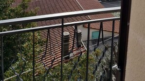 Un quartier résidentiel caractérisé par des toits recouverts de tuiles en terre cuite, un balcon orné d’une rambarde en métal et offrant une vue sur un paysage vallonné en arrière-plan.