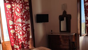 Une chambre à coucher comprenant un lit, une commode, un téléviseur fixé au mur et une fenêtre avec des rideaux.
