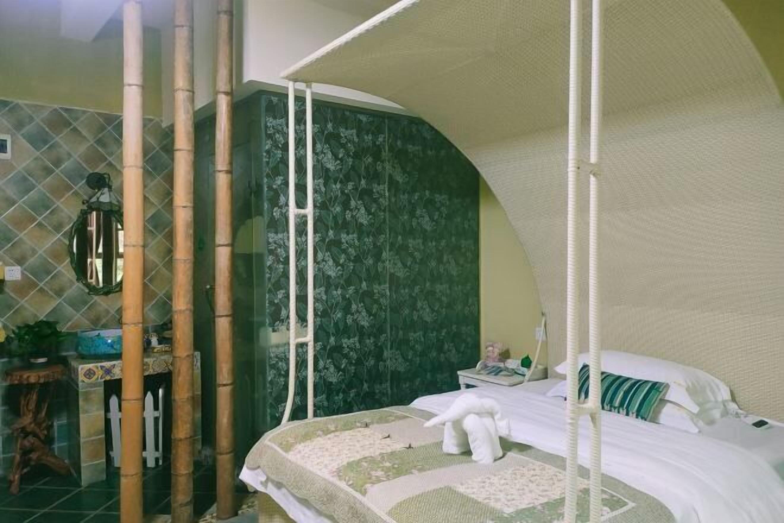 Un dormitorio con cama a dosel, papel tapiz floral verde y una mesita de noche con lámpara.