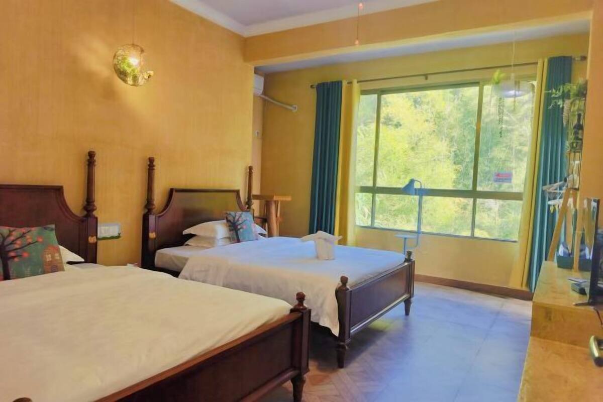 A hotel room with two beds, a large window with curtains, and a wooden headboard.