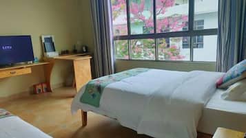A hotel room with a bed, a desk with a computer, a TV, and a window with a view of pink flowers.