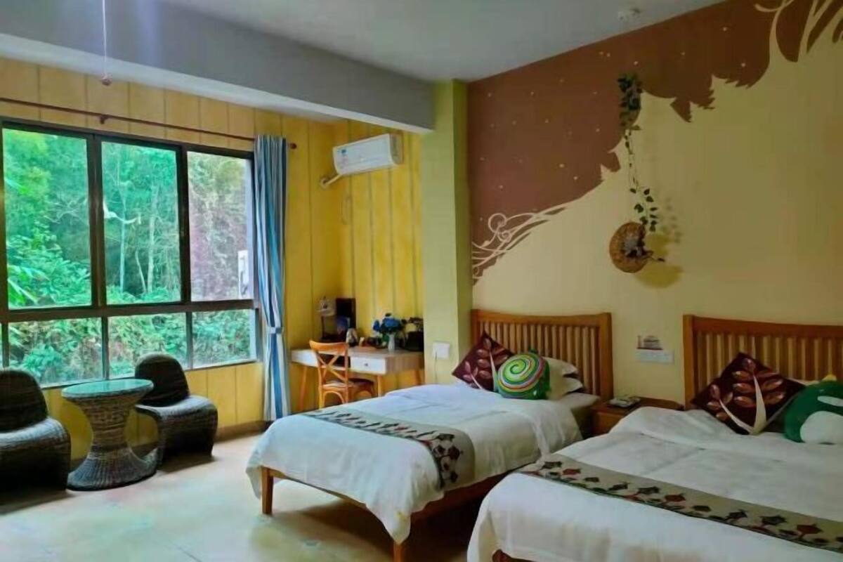 A room with two beds, a desk, a chair, and a large window with a view of greenery.