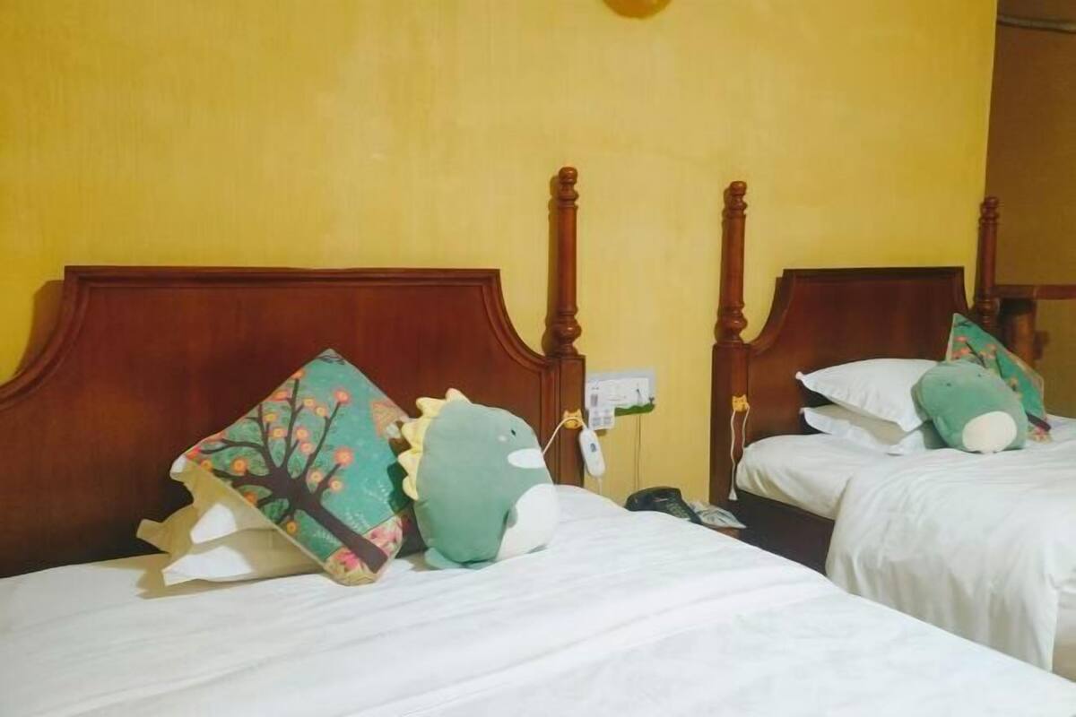 Two beds with wooden headboards, a green dinosaur-shaped pillow, and a telephone on the nightstand.