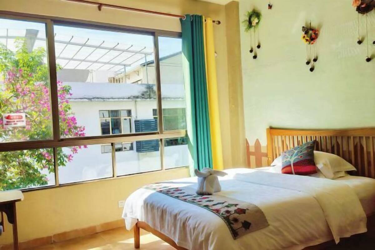A bedroom with a bed, a window, a curtain, and a view of the outside.
