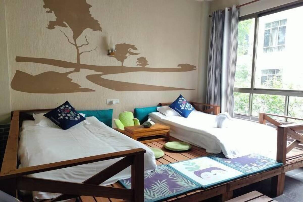 A room with two beds, a small table, and a view of the outdoors.
