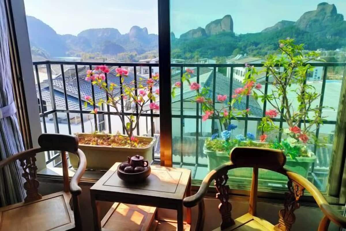 A balcony with a table, chairs, a teapot, and potted plants with flowers.