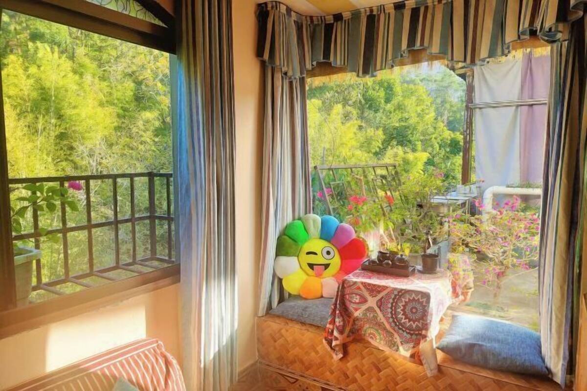 A balcony with a view of trees, a table with a patterned tablecloth, and a colorful flower decoration.