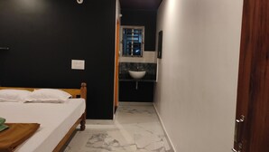 A bedroom with a bed, a nightstand, a window, and a bathroom with a sink and mirror. - Nature Valley Gokarna  (Kumta)