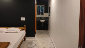 A bedroom with a bed, a nightstand, a window, and a bathroom with a sink and mirror. - Nature Valley Gokarna  (Kumta)
