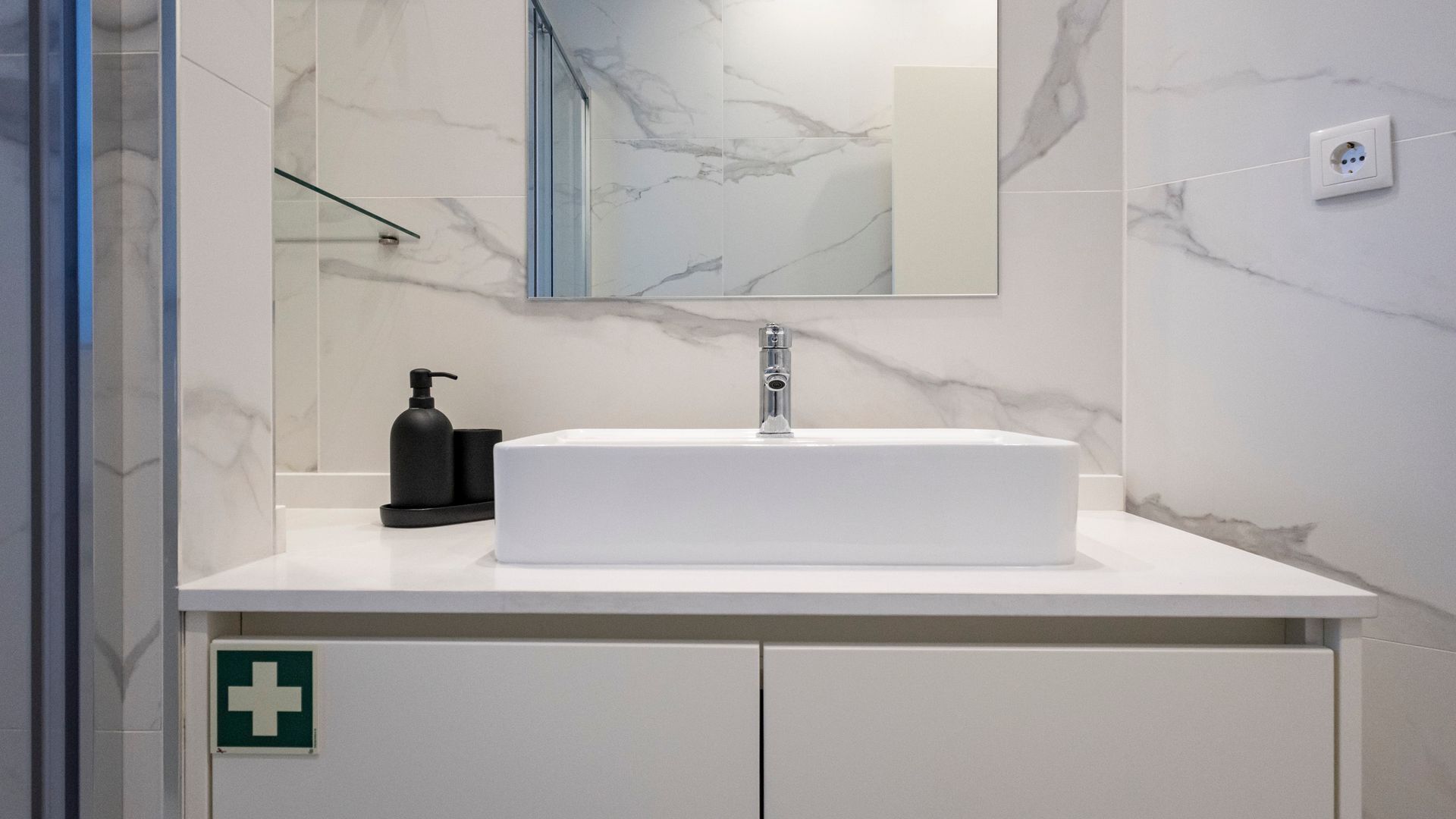 Een moderne badkamer met een witte wasbak, een spiegel en een marmeren achterwand.