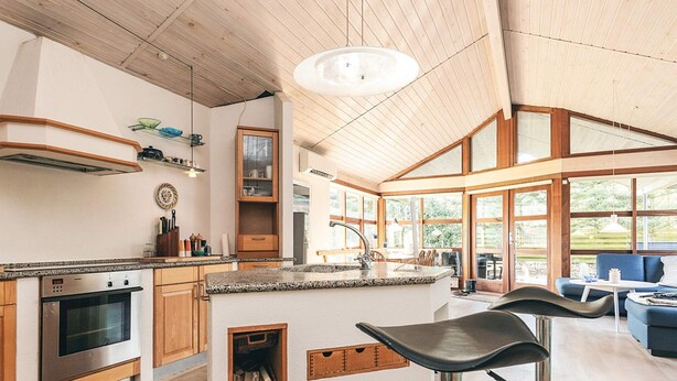 A modern kitchen with wooden cabinets, a stainless steel oven, and a bar area with stools. - 6 Person Holiday Home in Spottrup (Spøttrup)