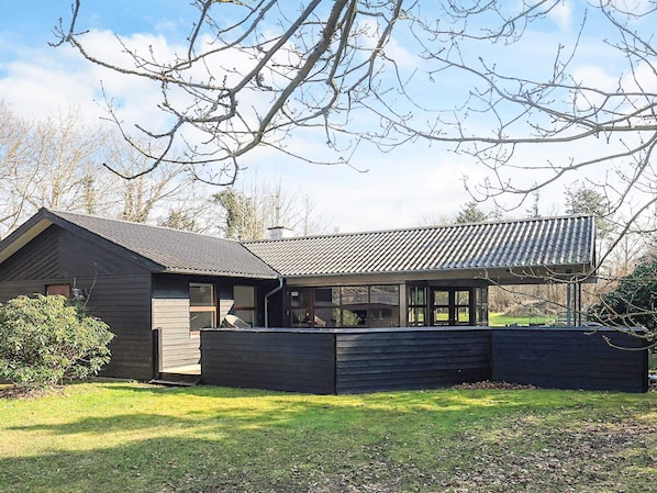 A modern house with a large glass window area, a dark exterior, and a well-maintained lawn.