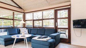 A modern living room with a blue sectional sofa, a small round table with a lamp, and a television mounted on the wall. - 6 Person Holiday Home in Spottrup (Spøttrup)