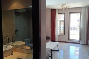 A modern bathroom with a large mirror, two sinks, and a toilet. There is a dining table and a window with curtains in the adjacent room. - Homeinn Pebble (Hohhot Chuangye Road International Mongolian Hospital) (Hohhot)