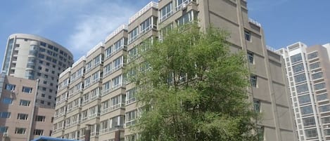 Un edificio de varios pisos con fachada plana, amplias ventanas y un árbol en primer plano.