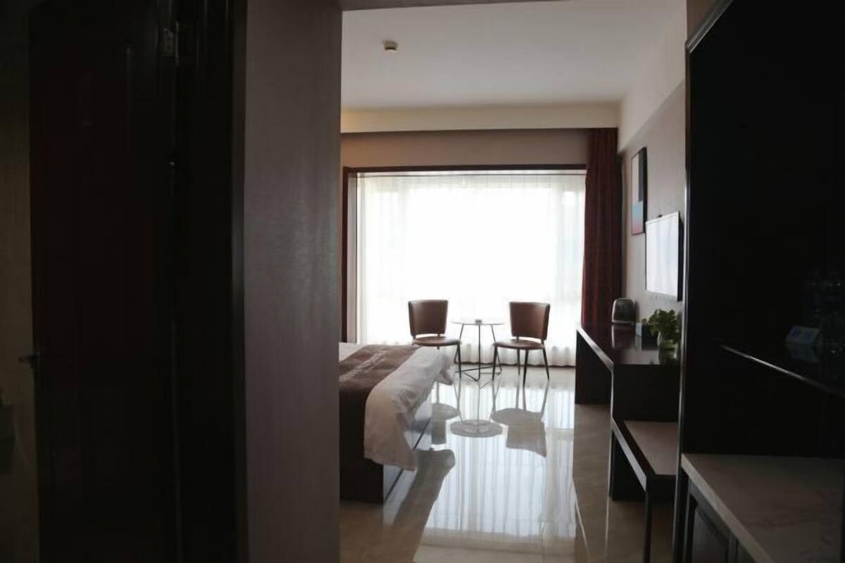 Quarto de hotel com cama, duas cadeiras, uma mesinha, televisão e varanda com cortinas.