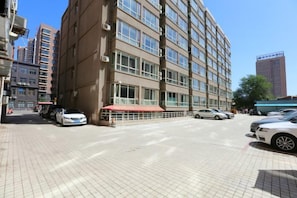A multi-story building with a red awning, parked cars, and a clear sky.