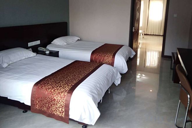 Two beds with white linens and brown decorative borders, a nightstand with a phone, and a wooden desk with chairs.
