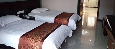 Two beds with white linens and brown decorative borders, a nightstand with a phone, and a wooden desk with chairs.