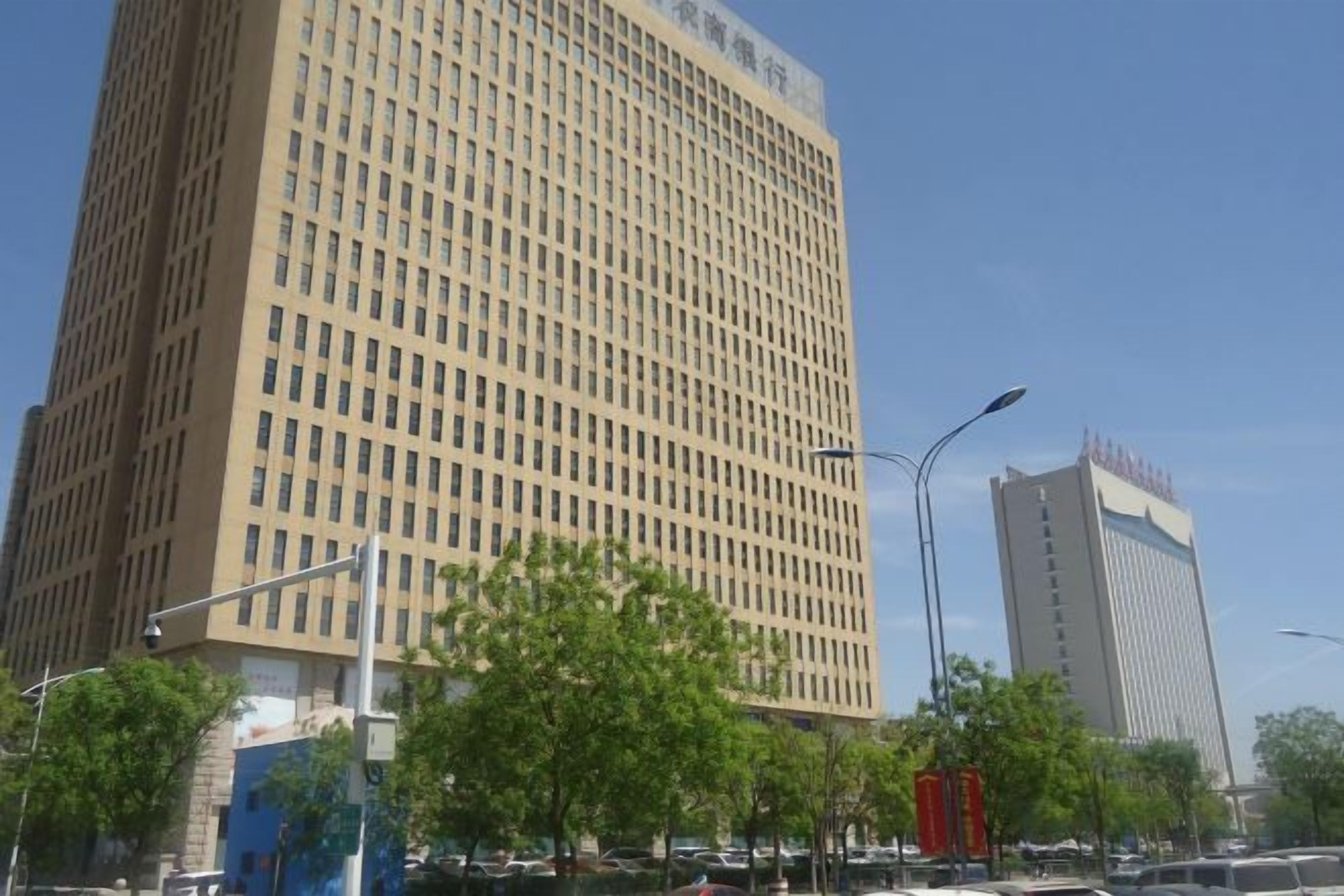 Un grand immeuble à la façade quadrillée, entouré d’arbres et de lampadaires.