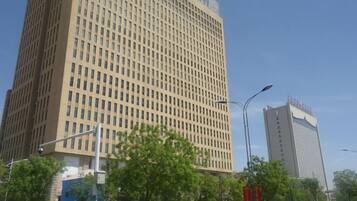 A tall building with a grid-like facade, surrounded by trees and street lamps.