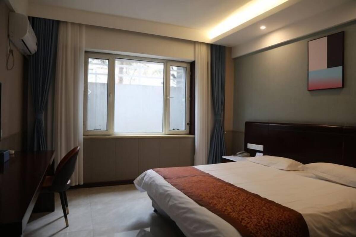 Quarto de hotel com cama, escrivaninha e janela com cortinas.